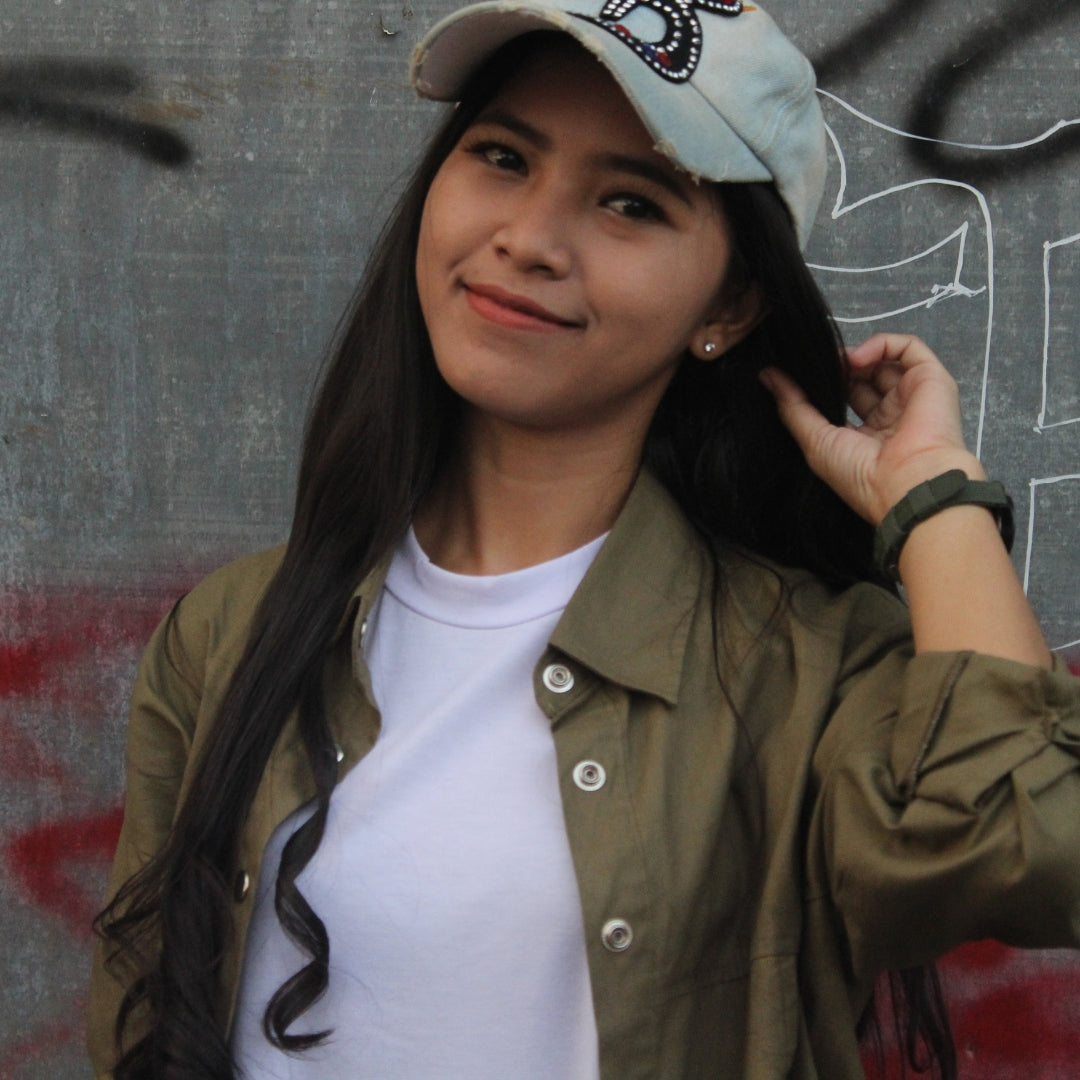 Woman wearing a cap and green jacket against a graffiti-covered wall