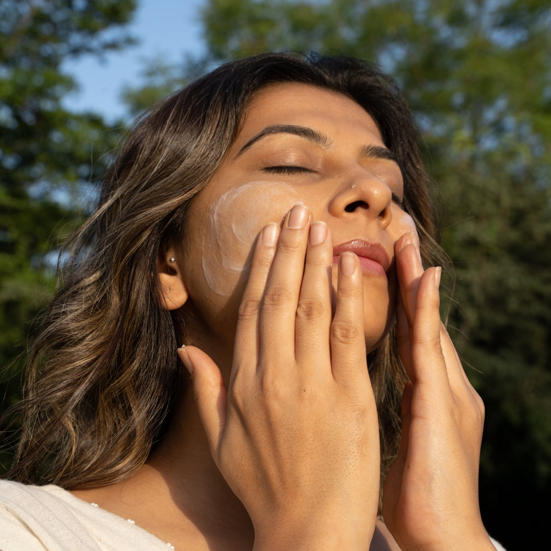 Woman applying sunscreen to her face outdoors with trees in the background